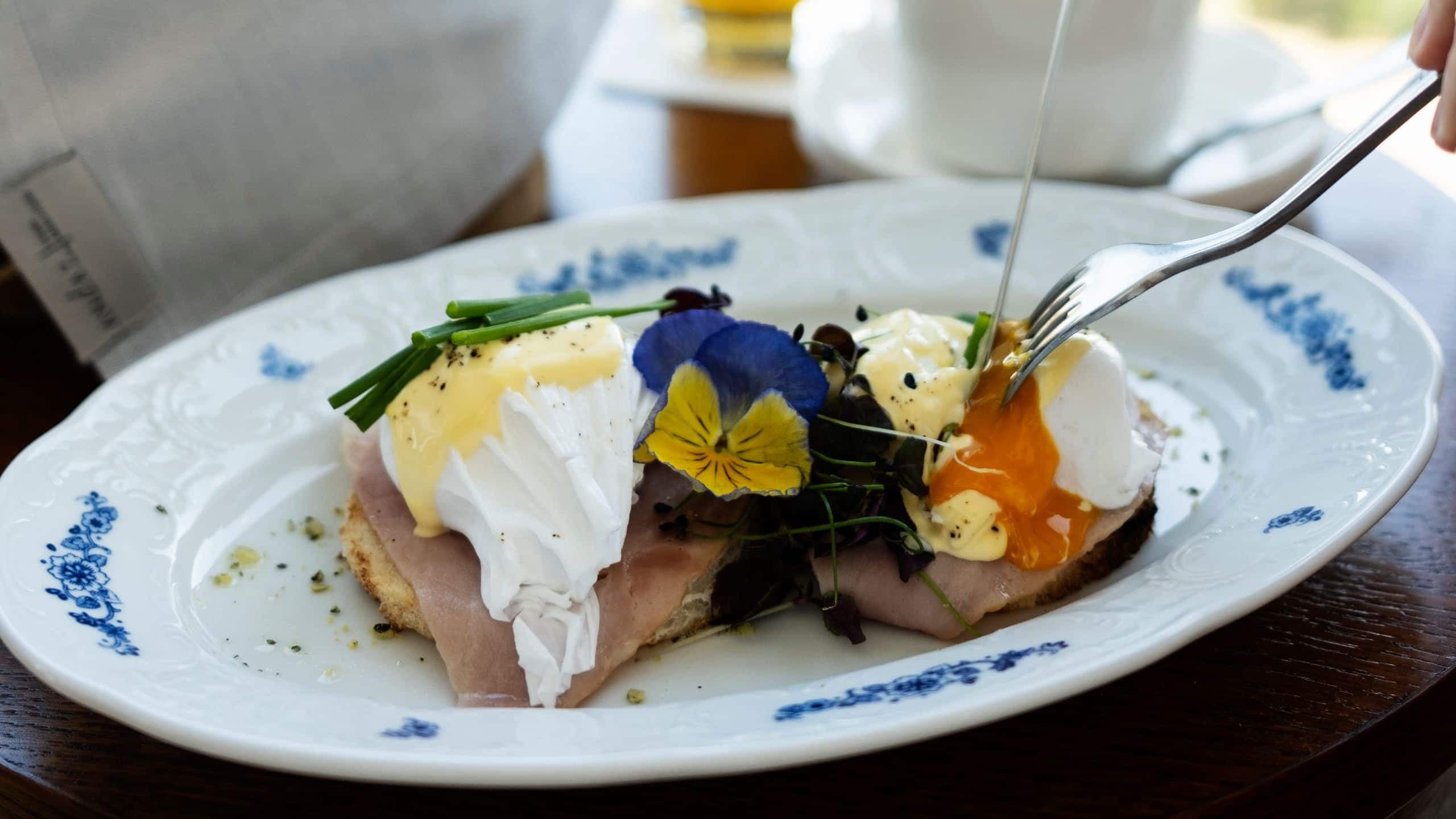 4 von 4 A delicate Eggs Benedict is being sliced, accompanied by freshly brewed coffee and orange juice